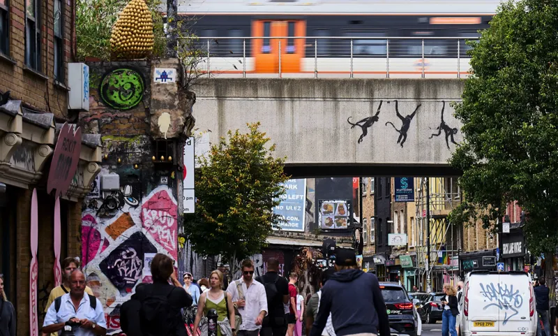 Three monkeys swinging from a bridge over Brick Lane.